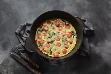 Frittata made of eggs, mushrooms, cherry tomatoes and spinach served in a pan. Italian cuisine