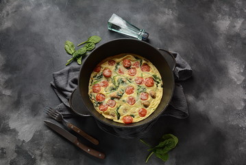 Frittata made of eggs, mushrooms, cherry tomatoes and spinach served in a pan. Italian cuisine