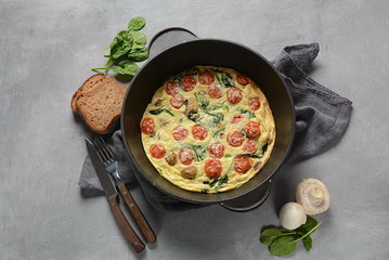 Frittata made of eggs, mushrooms, cherry tomatoes and spinach served in a pan. Italian cuisine.