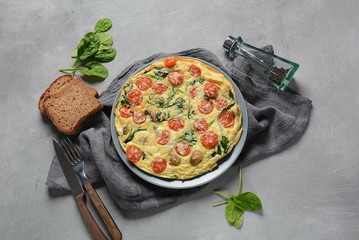 Frittata made of eggs, mushrooms, cherry tomatoes and spinach served on a plate. Italian cuisine