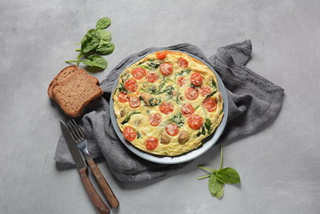 Frittata made of eggs, mushrooms, cherry tomatoes and spinach served on a plate. Italian cuisine. 