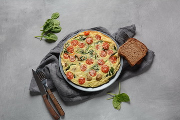 Frittata made of eggs, mushrooms, cherry tomatoes and spinach served on a plate. Italian cuisine. 