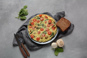 Frittata made of eggs, mushrooms, cherry tomatoes and spinach served on a plate. Italian cuisine. 