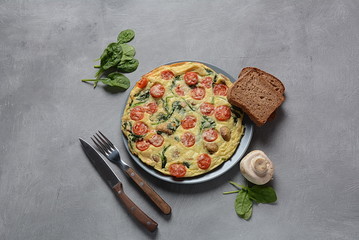 Frittata made of eggs, mushrooms, cherry tomatoes and spinach served on a plate. Italian cuisine