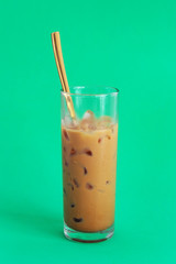 Glass of iced milk coffee with spoon on green background