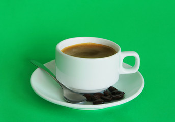 White coffee cup with spoon and coffee beans on green background