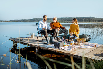 Man and woman with senior grandfather having a picnic with vegetables and fresh caught fish on the...