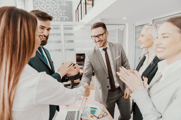 Two cheerful attractive Caucasian young business partners shaking hands in boardroom. Colleagues...