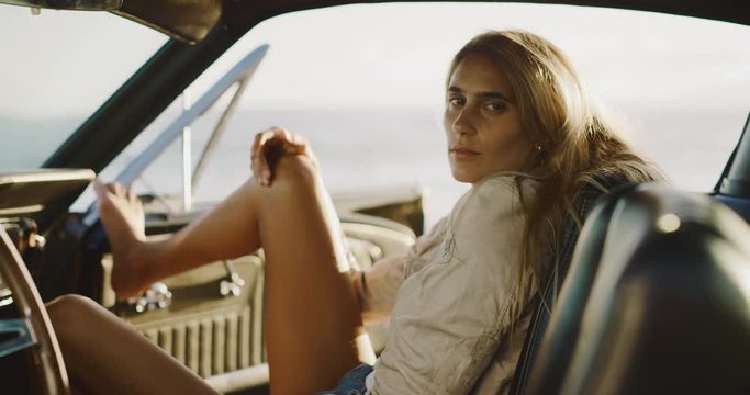 Attractive woman sitting in the passenger seat of a classic vintage car looking into the camera, model posing naturally in a vintage car, woman enjoying a coastal road trip