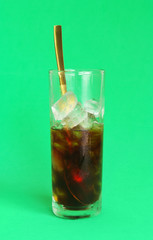 Iced coffee in glass and golden spoon on green background