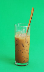 Glass of iced milk coffee with spoon on green background