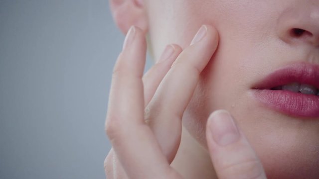 Close-up of innocent pure blonde girl touching her gentle shiny white skin on face with a hand.