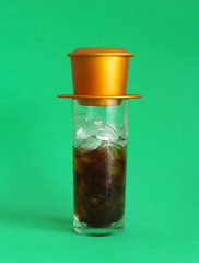 Vietnamese iced drip coffee in glass with phin on green background