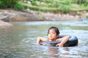 Asian child or kid girl with life ring from inner tube or tire for swimming and enjoy playing water with happy on stream or nature river in green jungle or garden forest for summer holiday relax