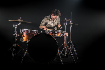 Professional drummer playing on drum set on stage on the black background