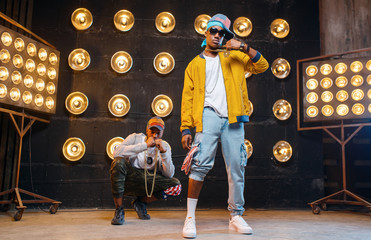 Rappers in caps dance on stage with spotlights
