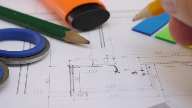 A young architect or designer is working on a project of a house or apartment, drawing pencil on paper. Pencil, ruler, marker and other stationery on the table