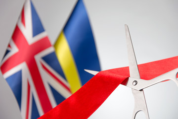 Ribbon cutting ceremony. Scissors cut red ribbon. .Ukraine and Union Jack bluered on the...