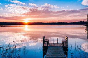 Idyllic view of the long pier with wooden bench on the lake. Sunset or sunrise over the water. - Powered by Adobe