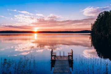 Idyllic view of the long pier with wooden bench on the lake. Sunset or sunrise over the water.