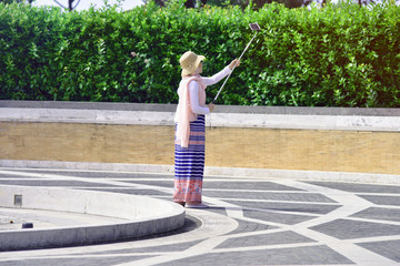 Obraz premium Fashionable beautiful young Muslim European girl in hijab and white shirt taking a selfie on smartphone outdoors in park on sunny day.