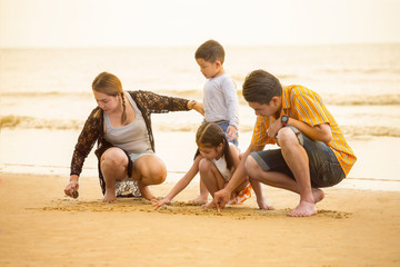 Happy asian family sitting on the beach drawing  in the sand together enjoying sunset in the summer leisure