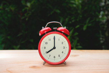 Red alarm clock on the wooden table with nature background