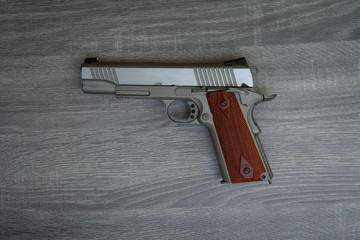 Stainless hand gun with brown hand grip is on the wooden floor  - begun