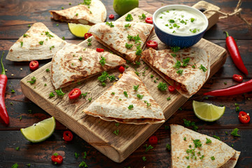Mexican quesadilla with chicken, corn, black beans, cheese, vegetables, lime and yogurt sauce on wooden board
