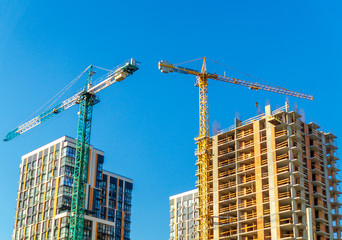 Fototapeta na wymiar Two construction cranes build houses on sky background.