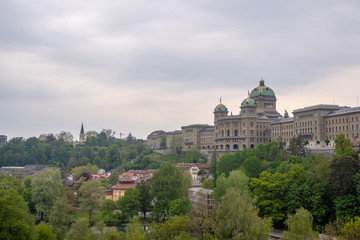 The Bundeshaus, parliament in bern , switzerland, with green trees foreground and cloudy sky background