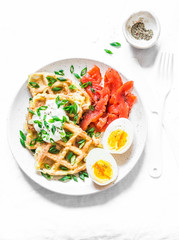 Crispy potato waffles with sour cream and green onions, smoked trout, boiled egg - delicious breakfast, snack, brunch on a light background, top view