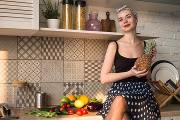 Girl in pin-up style sitting on kitchen table with pineapple in hand