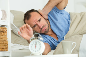 man in bed covering his ears from alarm clock noise