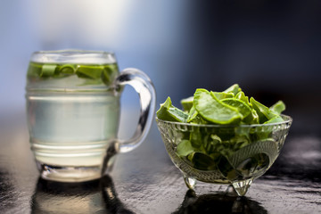 Close up of glass mug on wooden surface containing aloe vera detox drink in along with its entire raw ingredients with it. Horizontal shot with blurred background.