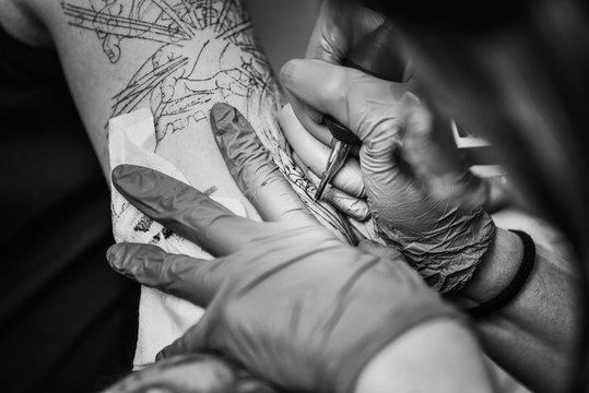 Black and white image of a tattoo artist starting to tattoo her client's arm