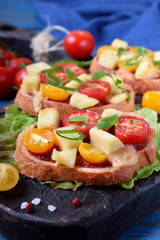 Bruschetta with different sorts of cherry tomatoes and soft cheese on the black board
