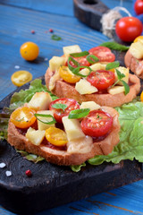 Bruschetta with different sorts of cherry tomatoes and soft cheese on the black board