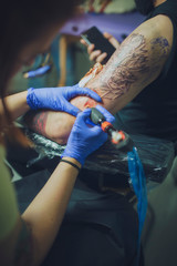 Detail of a professional tattoo artist tattooing the arm of a young client.