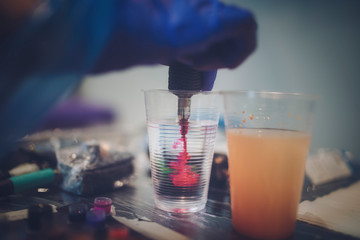 A tattooist cleans the needles of the tattoo machine in a glass of water to get another color