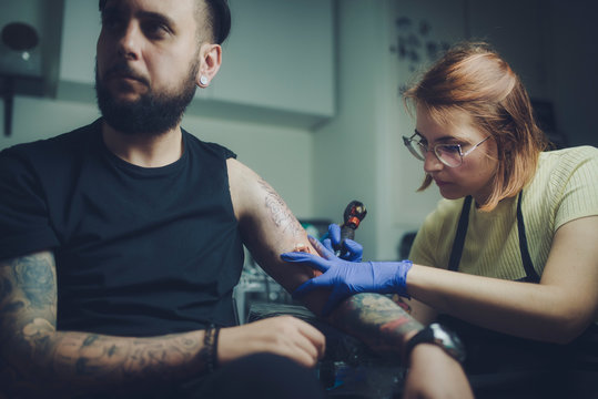 a professional tattooist woman makes a tattoo to a young man with a beard