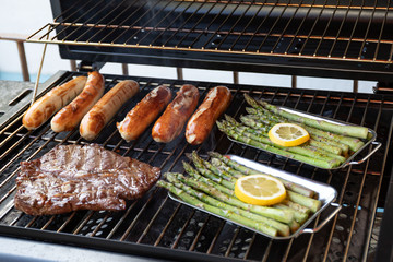 Würstchen, Steak und grüner Spargel auf dem Grill