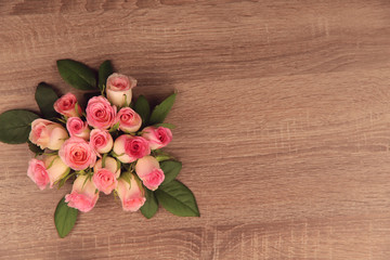 Obraz na płótnie Canvas Delicate bouquet of pink roses on a brown wooden background. Free space for text on the right. Background, close-up, horizontal. Holiday concept.