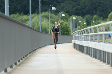 Junge Frau fährt mit Elektroroller auf Radweg über Brücke 2/2