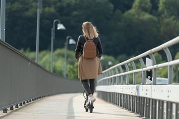 Junge Frau fährt mit Elektroroller auf Radweg über Brücke 2/2