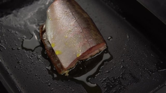 Large piece of red appetizing fish with spices fried in deep pan with non-stick coating, tracking shot.