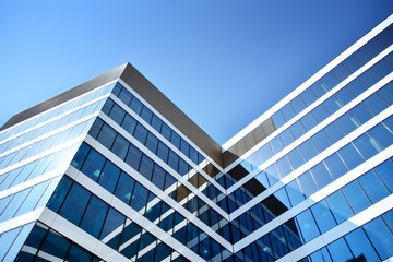 New office building in business center. Wall made of steel and glass with blue sky.  - Powered by Adobe