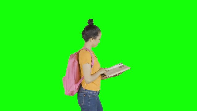 Young college student reading a book while carrying backpack and walking in the studio. Shot in 4k resolution with green screen background