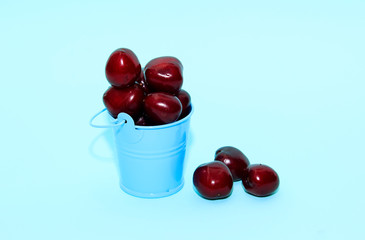 Fresh cherry in blue bucket on blue paper background. Fresh ripe cherries. Sweet cherries.