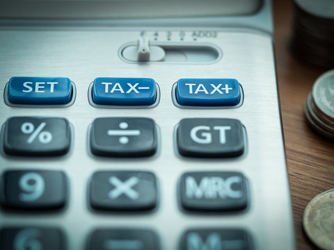 Tax cuts or reduce and tax increase concept, selective focus on TAX minus and TAX plus buttons on calculator with background of blurred coins.